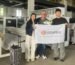 Technical specialists and Mexican textile entrepreneur posing for a commemorative photograph in front of the latest ultrasonic quilting machine model during a successful factory demonstration.